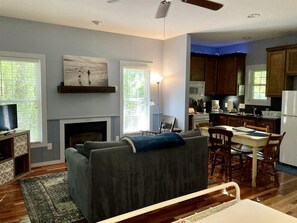 A living room with a sofa, a fireplace, a dining area with a table and chairs, and a kitchen with cabinets and appliances. - Secluded Woodland Cabin Rental with Hot Tub in Yadkin Valley Wine Region (Elkin)