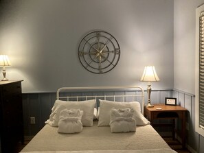Un dormitorio con una cama, lámparas de noche, un reloj de pared y una mesita con lámpara.