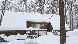 A snow-covered cabin with a visible window and door, surrounded by trees. - Charmingly Rustic Weekend Getaway in the Mountains near Pittsburgh, Pennsylvania (Champion)