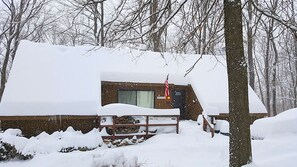 A snow-covered cabin with a visible window and door, surrounded by trees. - Charmingly Rustic Weekend Getaway in the Mountains near Pittsburgh, Pennsylvania (Champion)