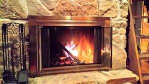 A stone fireplace with a metal frame, a fire burning inside, and a metal stand with a candle to the left. - Charmingly Rustic Weekend Getaway in the Mountains near Pittsburgh, Pennsylvania (Champion)