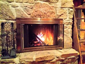 A stone fireplace with a metal frame, a fire burning inside, and a metal stand with a candle to the left. - Charmingly Rustic Weekend Getaway in the Mountains near Pittsburgh, Pennsylvania (Champion)