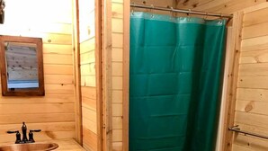 A wooden cabin bathroom with a sink, toilet, and green shower curtain.