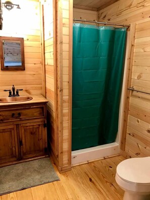 Une salle de bain rustique, aménagée dans une cabane en bois, avec un lavabo, des toilettes et un rideau de douche vert.