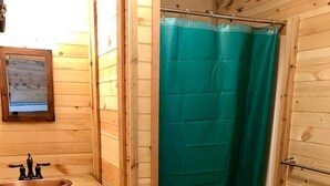 Baño de cabaña de madera con lavamanos, inodoro y cortina de ducha verde.