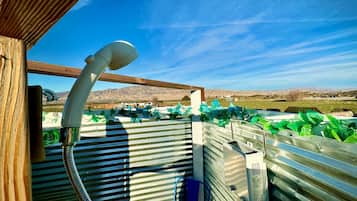 A metal-framed outdoor shower area with a hose, a blue chair, and a view of a mountainous landscape.