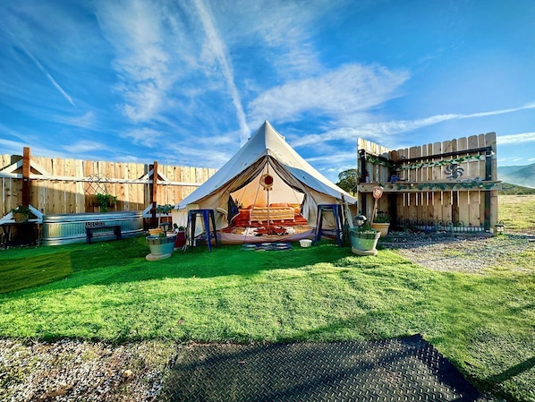 A tented accommodation with a grassy lawn, a metal bench, and a wooden fence.