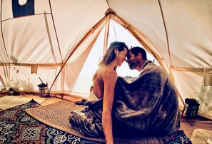 Une tente à l’intérieur de laquelle se trouvent un couple, assis, entourés de tapis et de plantes en pot.