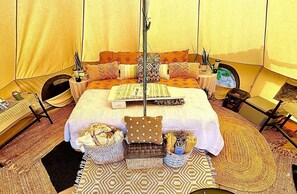 Une chambre spacieuse aménagée comme une tente, avec un grand lit, de nombreux oreillers, une table d’appoint, une chaise, une petite table et une radio.