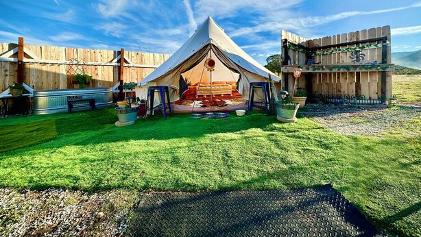 Un alloggio in tenda con prato, una panca in metallo e una recinzione in legno.