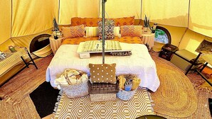 Un'ampia camera a tenda con un grande letto, numerosi cuscini, un tavolino, una sedia, un piccolo tavolo e una radio.