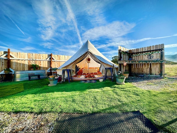A tented accommodation with a grassy lawn, a metal bench, and a wooden fence.