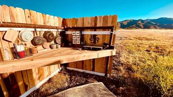 Un banco de madera con estructura metálica, rodeado por una valla de madera, ofrece una vista despejada de un paisaje montañoso al fondo.