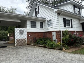 A two-story house with a covered porch, a brick foundation, and a gravel driveway.