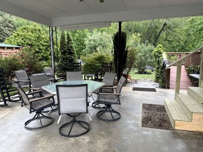 An outdoor patio with a table and chairs, surrounded by greenery and a wooden deck.
