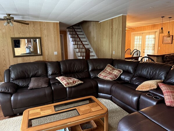 A living room with a sectional sofa, a wooden coffee table, a staircase, and wooden paneled walls.