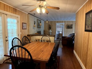 A dining area with a wooden table and chairs, a kitchen in the background, and a ceiling fan.