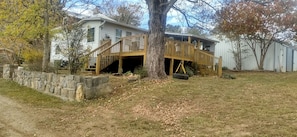 A two-story house with a wooden deck, stone wall, and a large tree in front. - Charming Farmhouse Glamping Cabin in Sparta, Tennessee (Sparta)