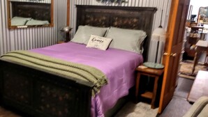 Ein Schlafzimmer mit Bett, Nachttisch, Lampe, Spiegel und Tür.