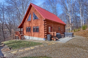 A log cabin with a red roof, a porch, and a grill area.