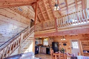 A wooden cabin interior with a kitchen, dining area, and a staircase leading to an upper level.