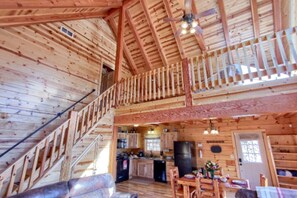 A wooden cabin interior with a kitchen, dining area, and a staircase leading to an upper level. - Beautiful Cabin Retreat near Hocking Hills, For Peaceful Getaways in Ohio (Logan)