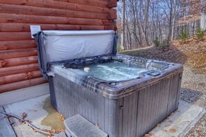A hot tub outside a log cabin with a wooden deck and a natural forest backdrop.