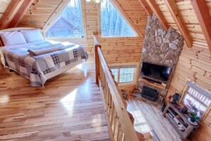 Ein gemütliches Blockhaus mit Holzeinrichtung, einem Steinkamin, einem Bett mit karierter Decke und einem Fernseher.
