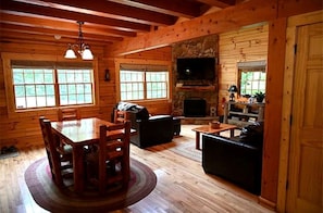 Ein Blockhaus-Interieur mit Essbereich, Sitzgelegenheiten, Kamin und Fernseher.