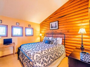 A bedroom with a wooden log wall, a bed with patterned bedding, a desk with a computer, and two bedside lamps. - Delightful Weekend Getaway for the Perfect Outdoor Experience near Mansfield, Ohio (Fredericktown)