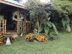 A wooden structure with a porch, surrounded by a garden with orange flowers and a birdbath. - Idyllic Tiny House Rental on a Peaceful Farm in Middle Tennessee (Sparta)