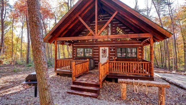 A wooden cabin with a porch, a fireplace, and a window. - Romantic Getaways to this Rustic Cabin Rental with Stone Fireplace in Logan, Ohio (Logan)