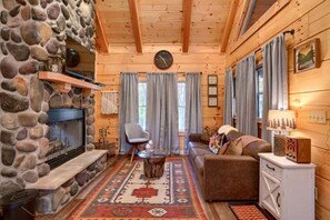 A log cabin interior with a stone fireplace, a sofa, a chair, and a rug.