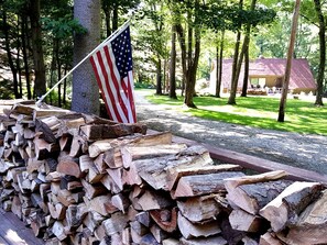A stack of firewood with an American flag, a gravel path, and a building in the background.