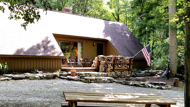 Una cabaña rústica con cimientos de piedra, una terraza de madera y una mesa de picnic al frente.