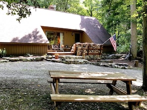 Una cabaña rústica con cimientos de piedra, una terraza de madera y una mesa de picnic al frente.