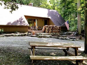Una cabaña rústica con cimientos de piedra, una terraza de madera y una mesa de picnic al frente.