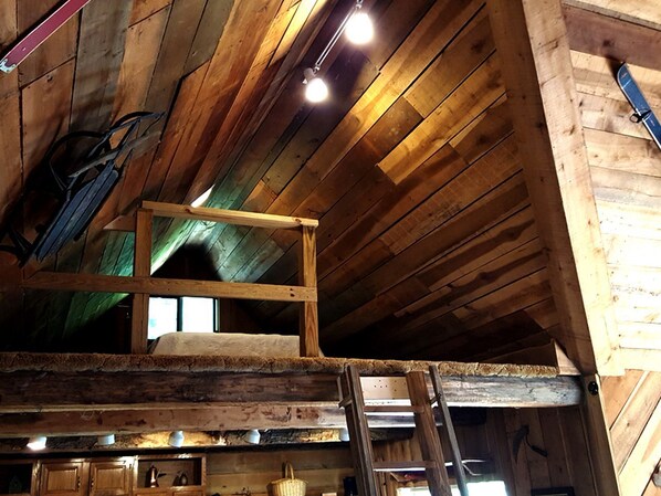 A wooden interior with a loft bed, wooden beams, and a ladder.