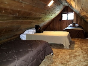 A small attic bedroom with two beds, a wooden ceiling, and a window.