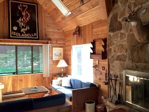 A rustic cabin interior with wooden walls, a stone fireplace, a sofa, a table, and a poster on the wall. - Family-Friendly Cabin Rental Nestled Among the Mountains of Champion, Pennsylvania (Champion)