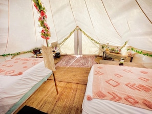 Een tent met twee bedden, een vloerkleed in het midden en een kleine tafel met een plant.