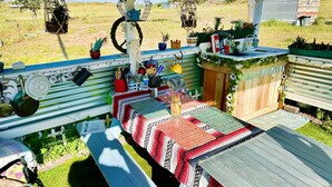 Un espace extérieur abrité, aménagé pour les repas, avec une longue table, des plantes suspendues et une clôture en bois rustique.
