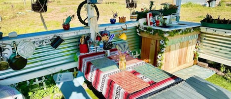 Un área de comedor al aire libre techada con una mesa larga, plantas colgantes y una valla de madera rústica.
