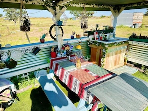 Un área de comedor al aire libre techada con una mesa larga, plantas colgantes y una valla de madera rústica.