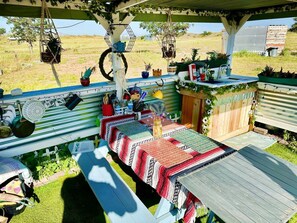 A covered outdoor dining area with a long table, hanging plants, and a rustic wooden fence. - Glamorous California Campsite Retreat with Great Views (New Cuyama)