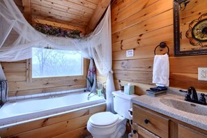A wooden cabin bathroom with a window, toilet, sink, and vanity. - Wonderful Ohio Getaways in this Wonderful Cabin Rental with Hot Tub (Logan)