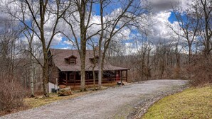 A rustic cabin with a porch, surrounded by trees and a gravel driveway. - Wonderful Ohio Getaways in this Wonderful Cabin Rental with Hot Tub (Logan)