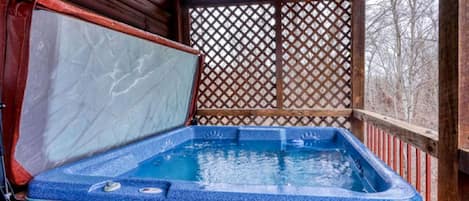 A hot tub in a wooden cabin with a lattice screen, a wooden deck, and a view of bare trees.