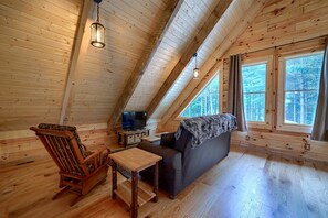 Ein gemütlicher Dachbodenraum mit Holzwänden, einer Couch, einem Fernseher und einem Holzstuhl.