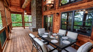 Une terrasse en bois avec une table et des chaises en verre, un pilier en pierre et de grandes fenêtres.